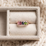 Rose gold five-stone oval gemstone ring resting elegantly inside a soft cream fabric jewelry box.