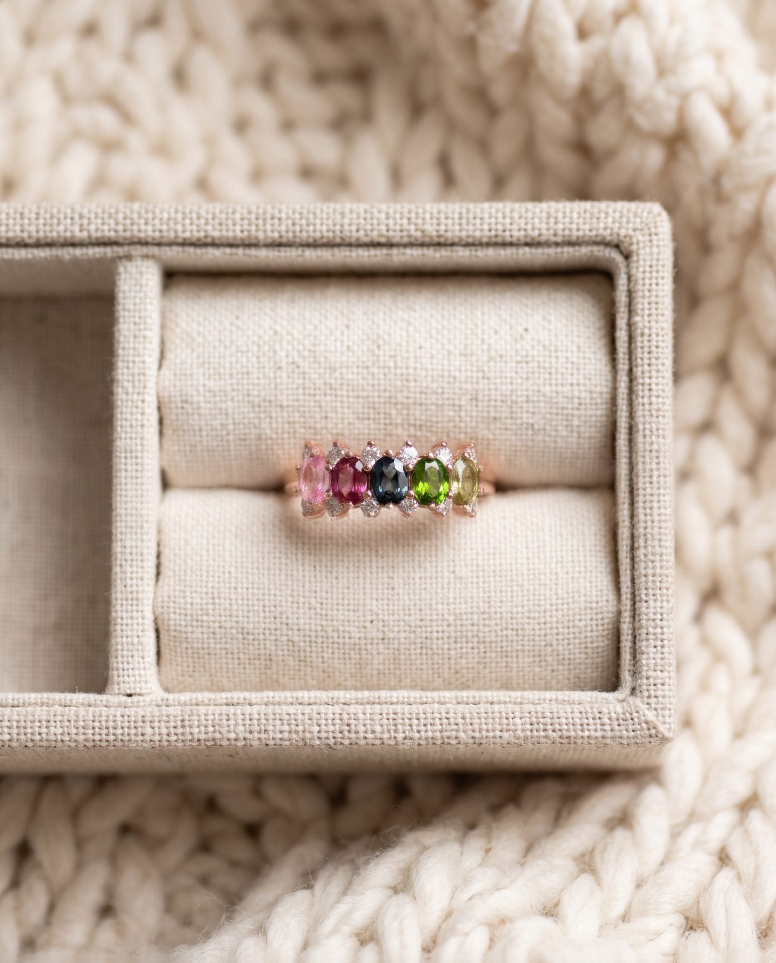 Rose gold five-stone oval gemstone ring resting elegantly inside a soft cream fabric jewelry box.