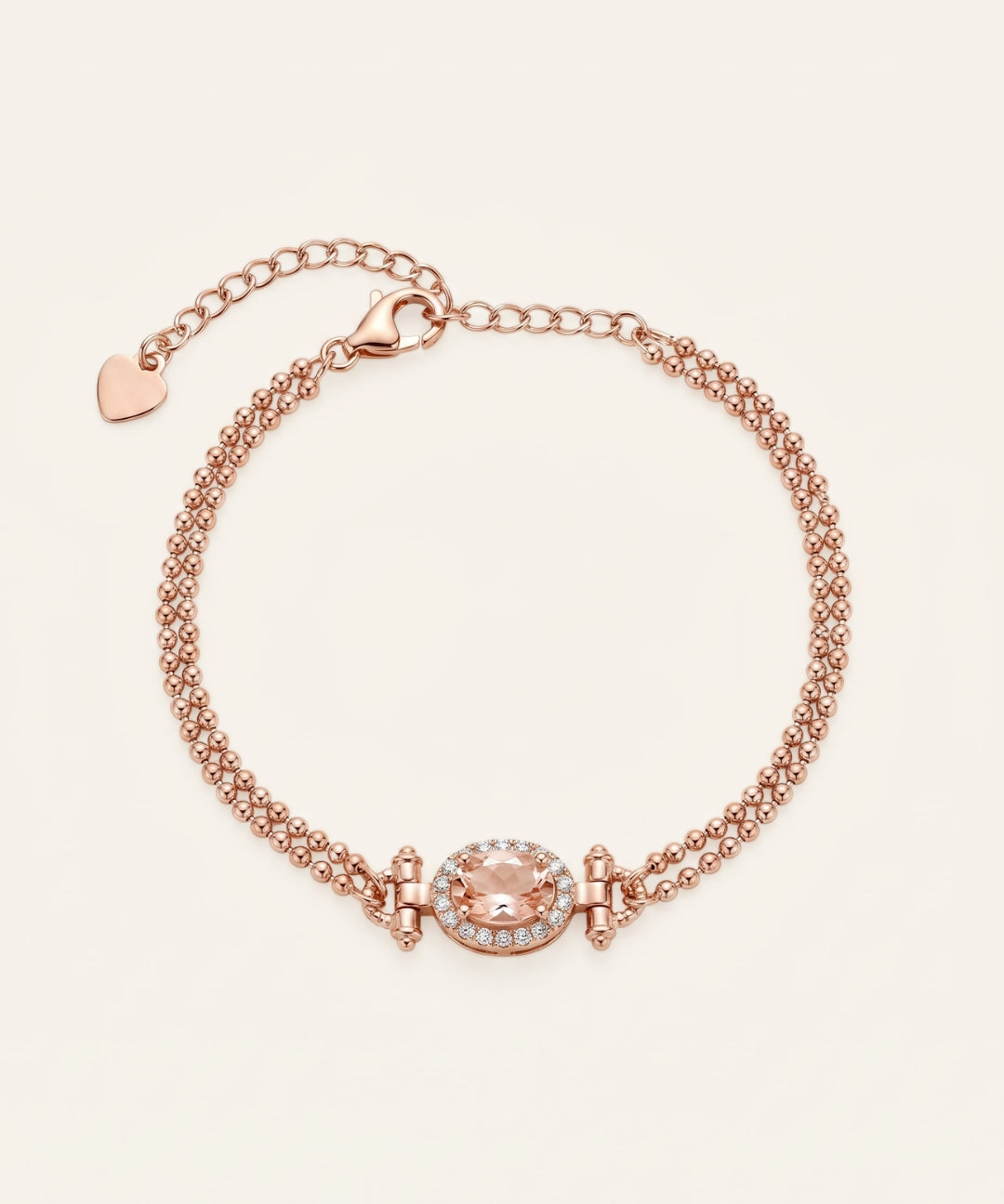 A studio product image of the Constance Petite Morganite Bracelet in rose gold, showcasing the natural peach-pink gemstone and the delicate heart charm at the end of the extension chain.
