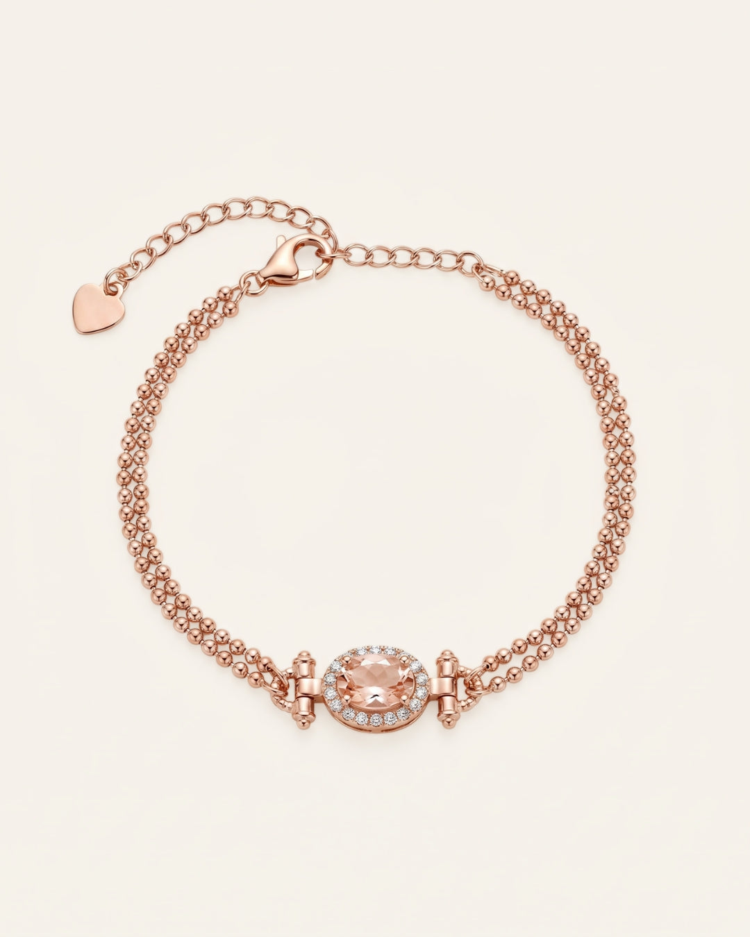 A studio product image of the Constance Petite Morganite Bracelet in rose gold, showcasing the natural peach-pink gemstone and the delicate heart charm at the end of the extension chain.