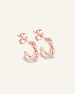 Criss-Cross Studs in rose gold, resting on a warm linen background