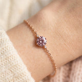 Overhead wrist shot of a dainty rose gold chain bracelet centering a fiery 1-carat rose pink solitaire gem flanked by two tiny accent stones.