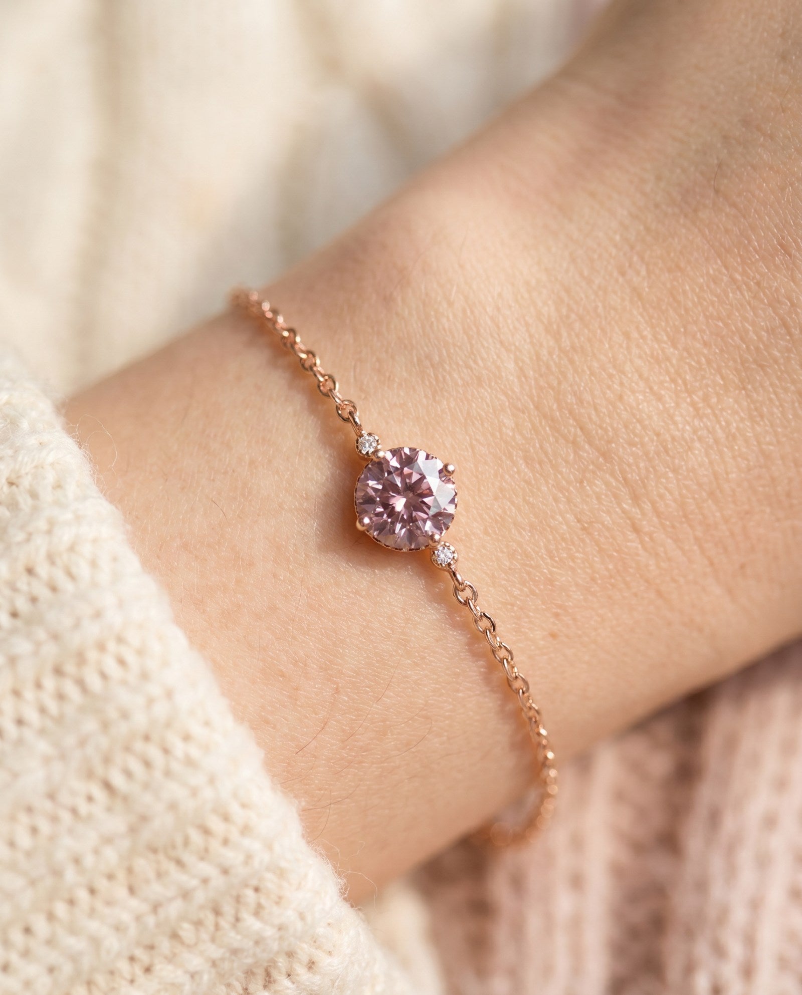 Overhead wrist shot of a dainty rose gold chain bracelet centering a fiery 1-carat rose pink solitaire gem flanked by two tiny accent stones.