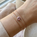 Layered wrist stack featuring a minimalist rose gold cuff, a delicate cable chain, and a round 1ct rose pink moissanite solitaire bracelet.