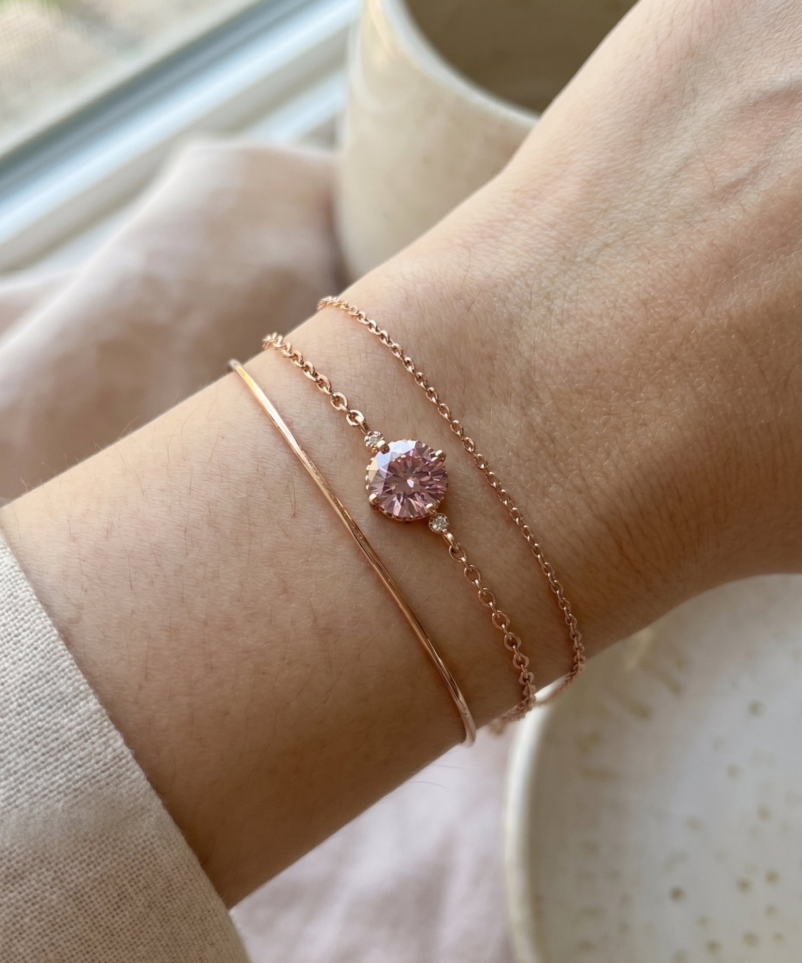 Layered wrist stack featuring a minimalist rose gold cuff, a delicate cable chain, and a round 1ct rose pink moissanite solitaire bracelet.