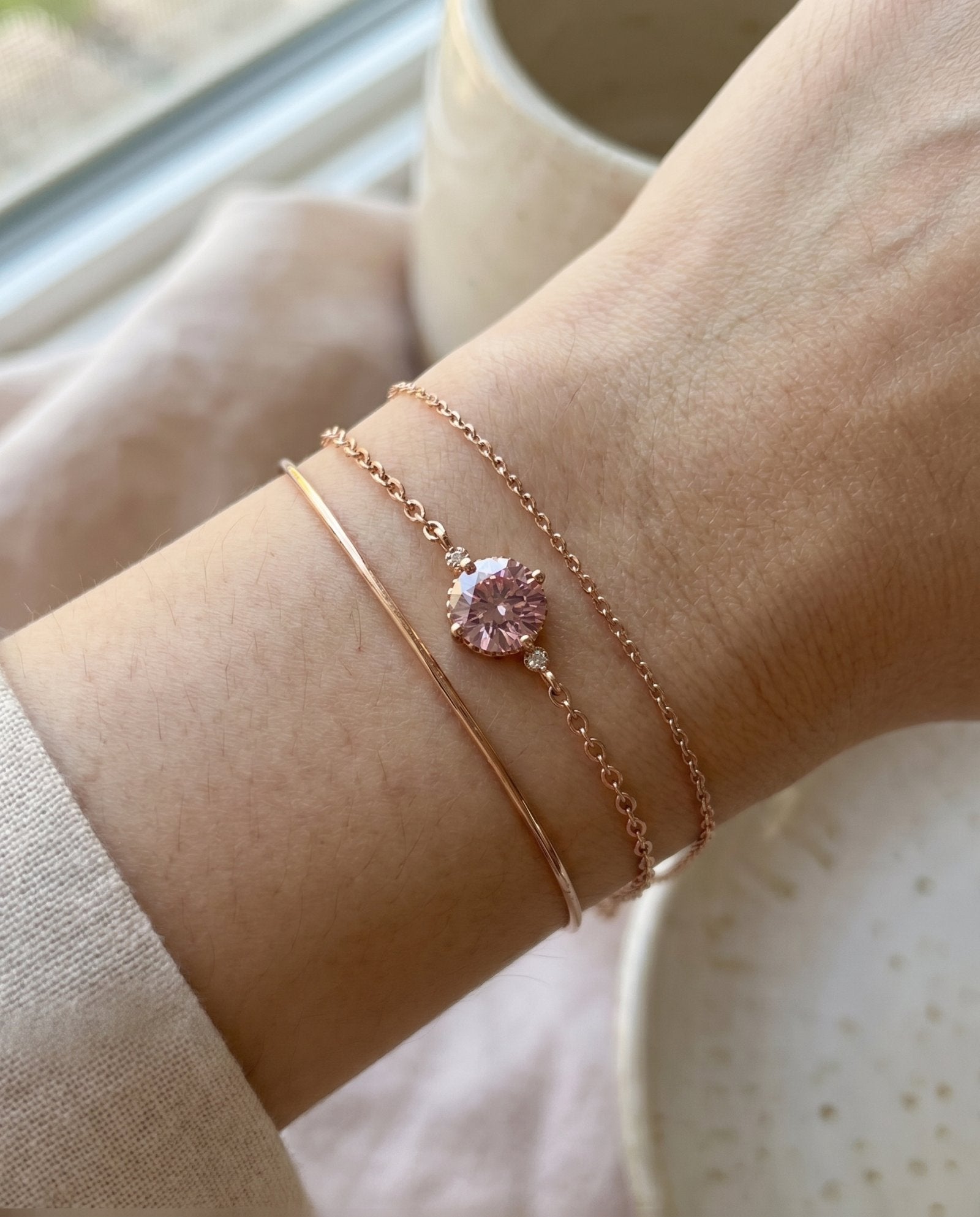 Layered wrist stack featuring a minimalist rose gold cuff, a delicate cable chain, and a round 1ct rose pink moissanite solitaire bracelet.