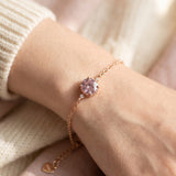 Side view profile of a model wearing a delicate 18k rose gold vermeil bracelet with a round brilliant pink moissanite stone in a scalloped crown setting.