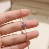 Hand holding a dainty rose gold chain bracelet to showcase the brilliant fire and details of the round 1-carat pink center stone and scalloped basket setting.