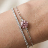 Close-up of a model wearing a dainty silver cable chain bracelet featuring a round-cut rose pink solitaire gemstone, stacked next to a sparkling diamond tennis bracelet.