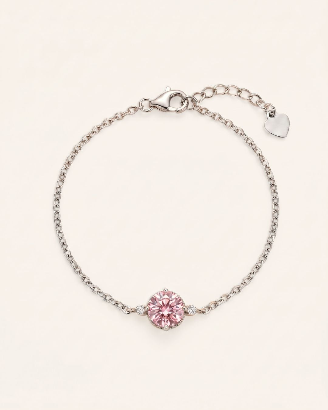 Flat lay view of a 925 sterling silver solitaire bracelet featuring a 1ct round brilliant rose pink moissanite stone, an adjustable extender chain, and a small heart charm.