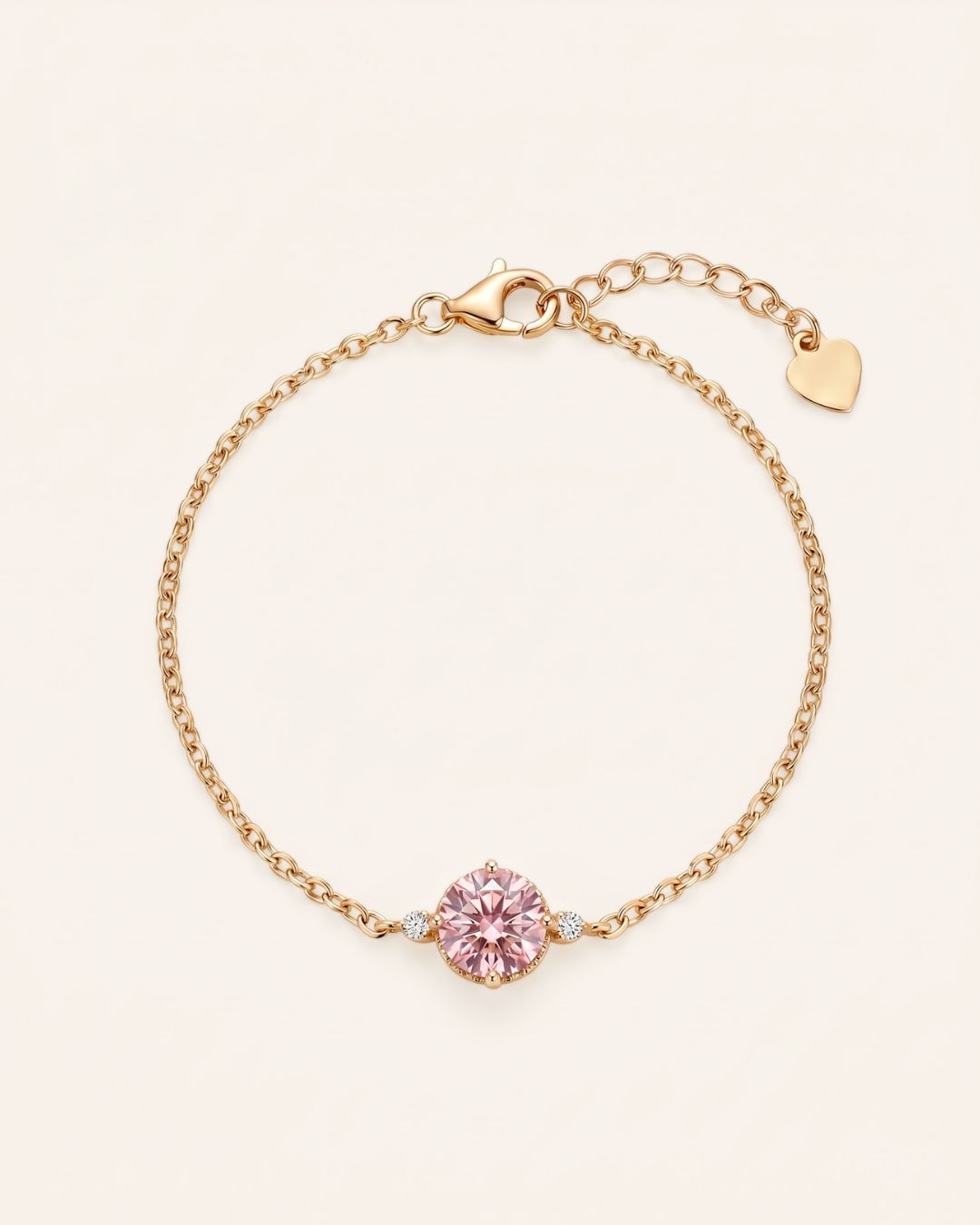 Flat lay view of a 18k yellow gold plated solitaire chain bracelet with a round-cut pink gemstone center and a heart-shaped tag on the adjustable extender clasp.