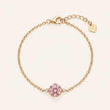 Flat lay view of a 18k yellow gold plated solitaire chain bracelet with a round-cut pink gemstone center and a heart-shaped tag on the adjustable extender clasp.