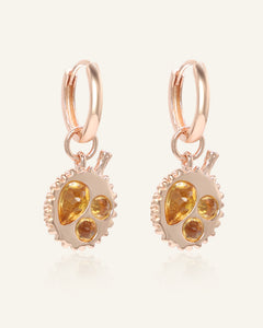Close-up of the Durian Citrine Huggies in rose gold, resting on a warm linen background