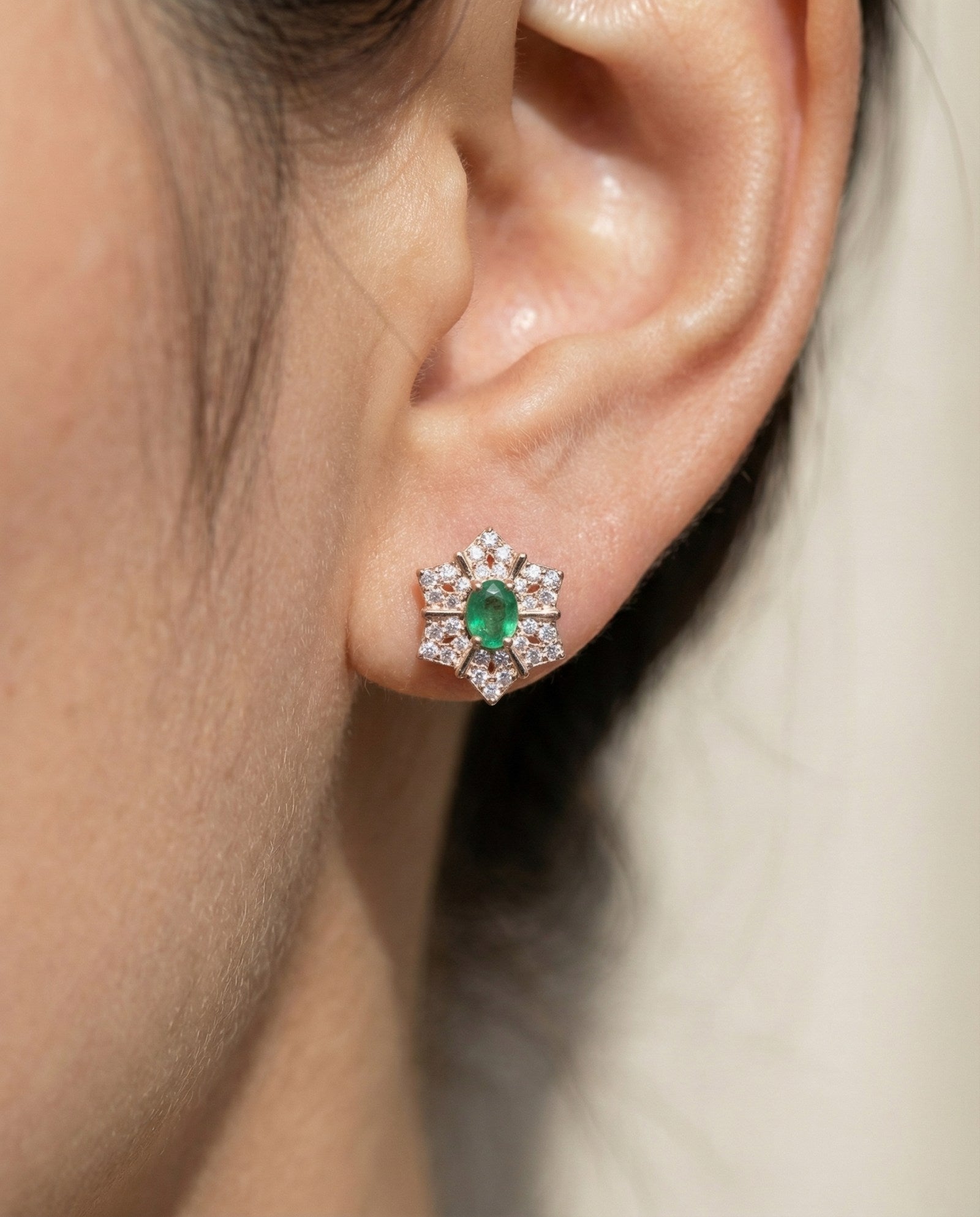 Close-up of a model wearing the Emerald Starflower Studs in rose gold, highlighting the vibrant natural emerald center.