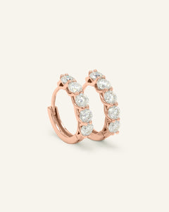 Close-up of the Entwine Huggies | White, Elate in rose gold, resting on a warm linen background