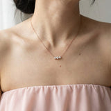 Lifestyle shot of the Everglow Trilogy Necklace in rose gold, showcasing the elegant graduated 'smile' silhouette on the neckline.