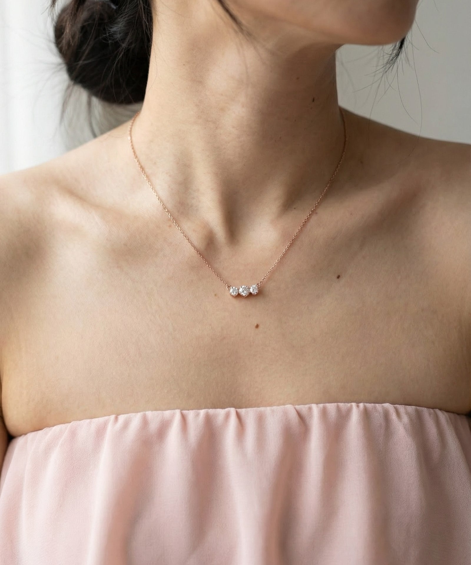 Lifestyle shot of the Everglow Trilogy Necklace in rose gold, showcasing the elegant graduated 'smile' silhouette on the neckline.