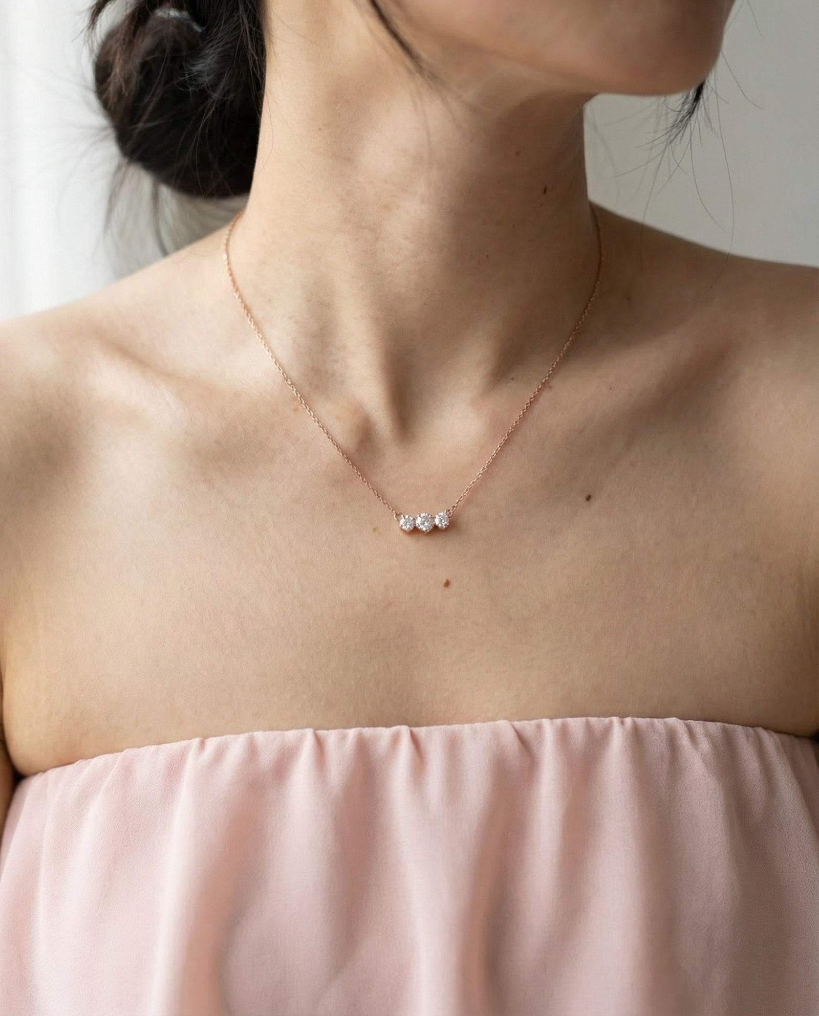 Lifestyle shot of the Everglow Trilogy Necklace in rose gold, showcasing the elegant graduated 'smile' silhouette on the neckline.