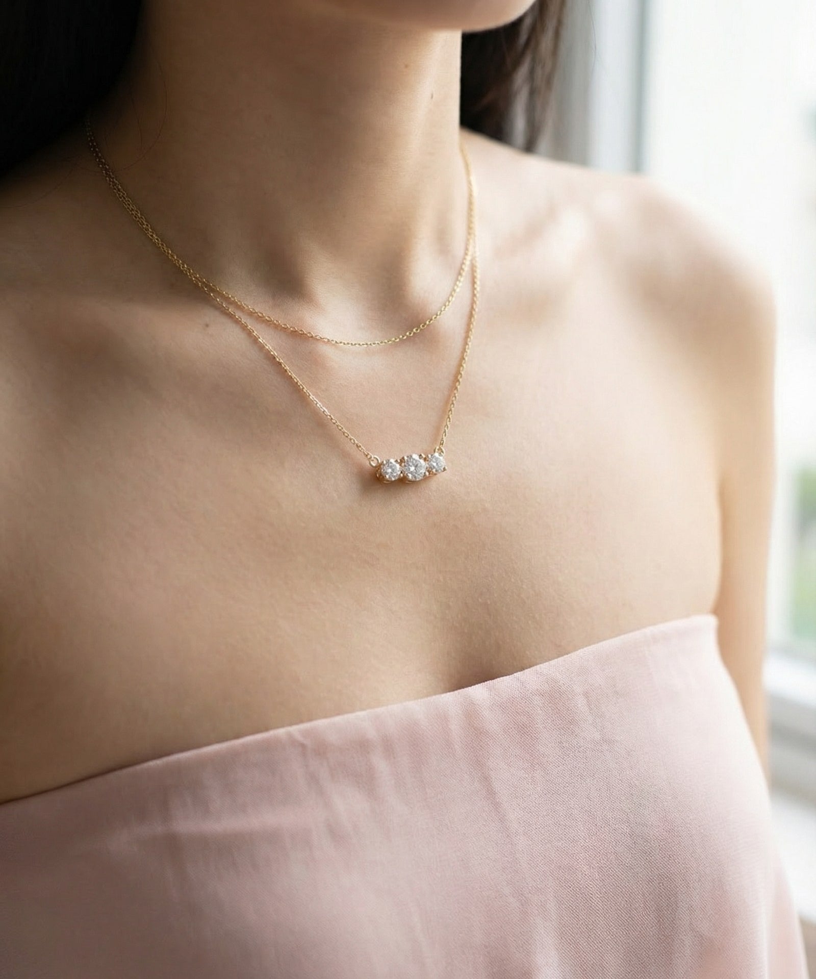 Close-up of a model wearing the Everglow Trilogy Moissanite Necklace in yellow gold, layered with a simple gold chain.