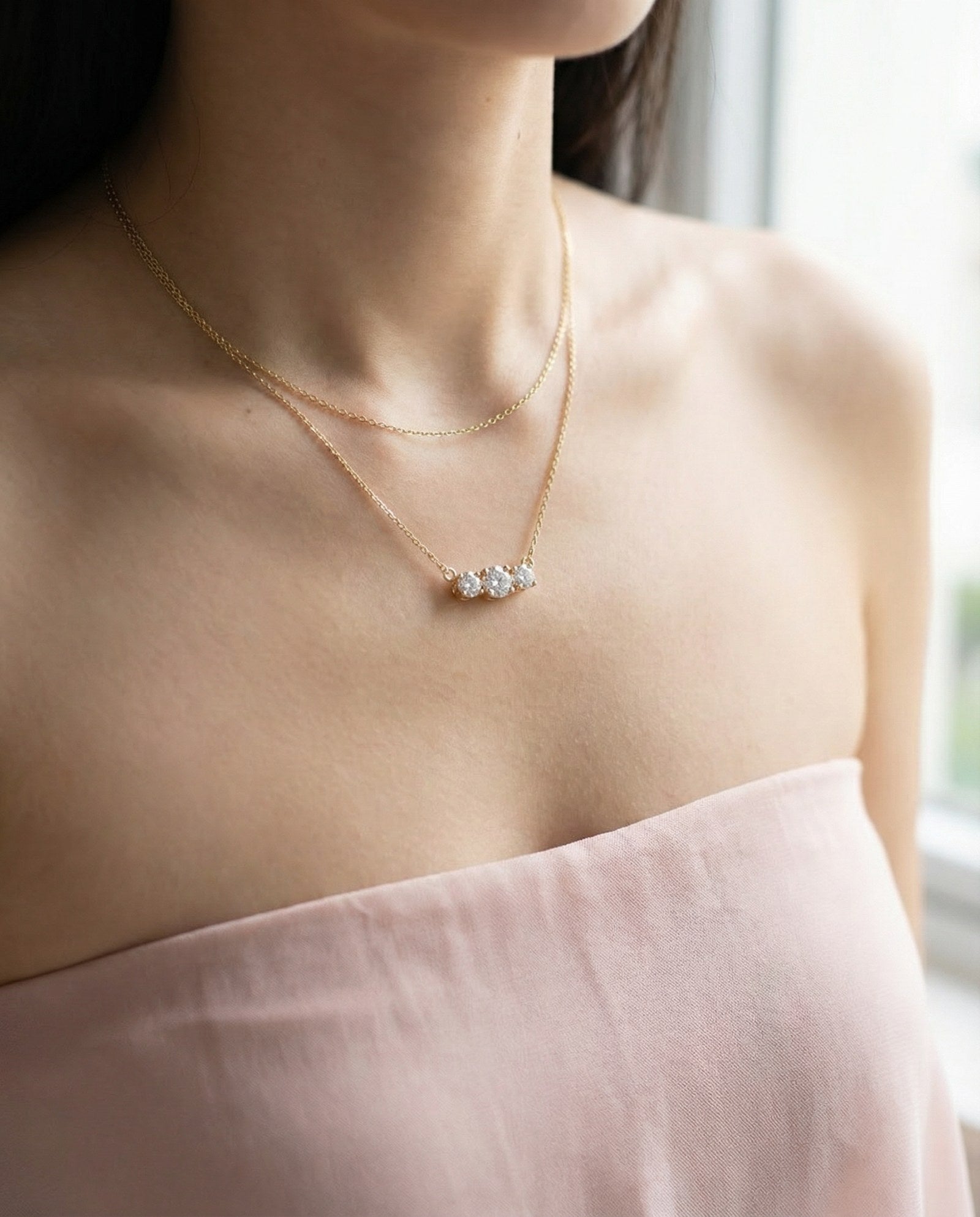 Close-up of a model wearing the Everglow Trilogy Moissanite Necklace in yellow gold, layered with a simple gold chain.