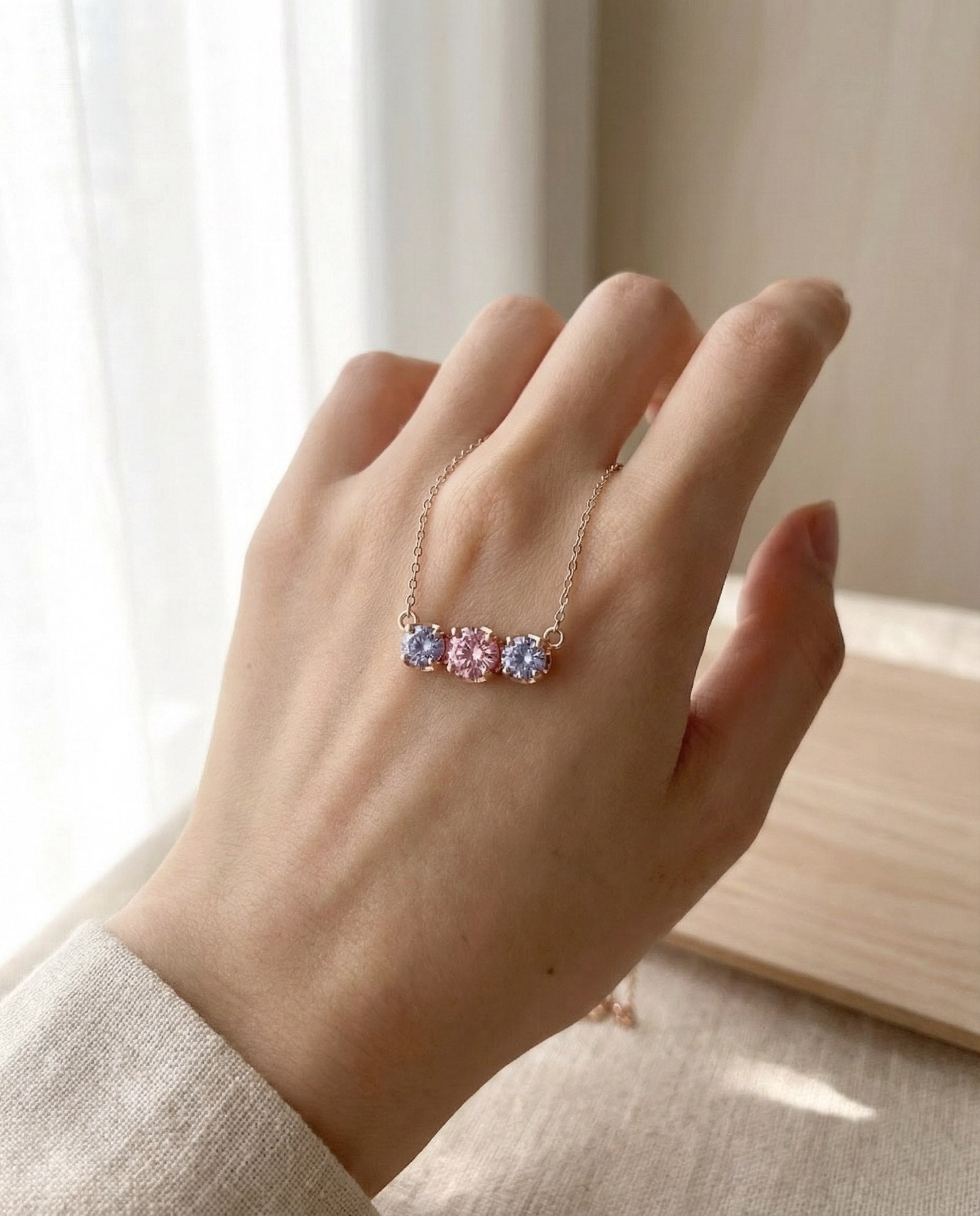 Everglow Trilogy Necklace in silver styled in a luxury cream jewelry box with a blurred soft pink background.