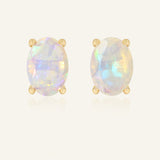 Prism Opal Studs in yellow gold, resting on a warm linen background