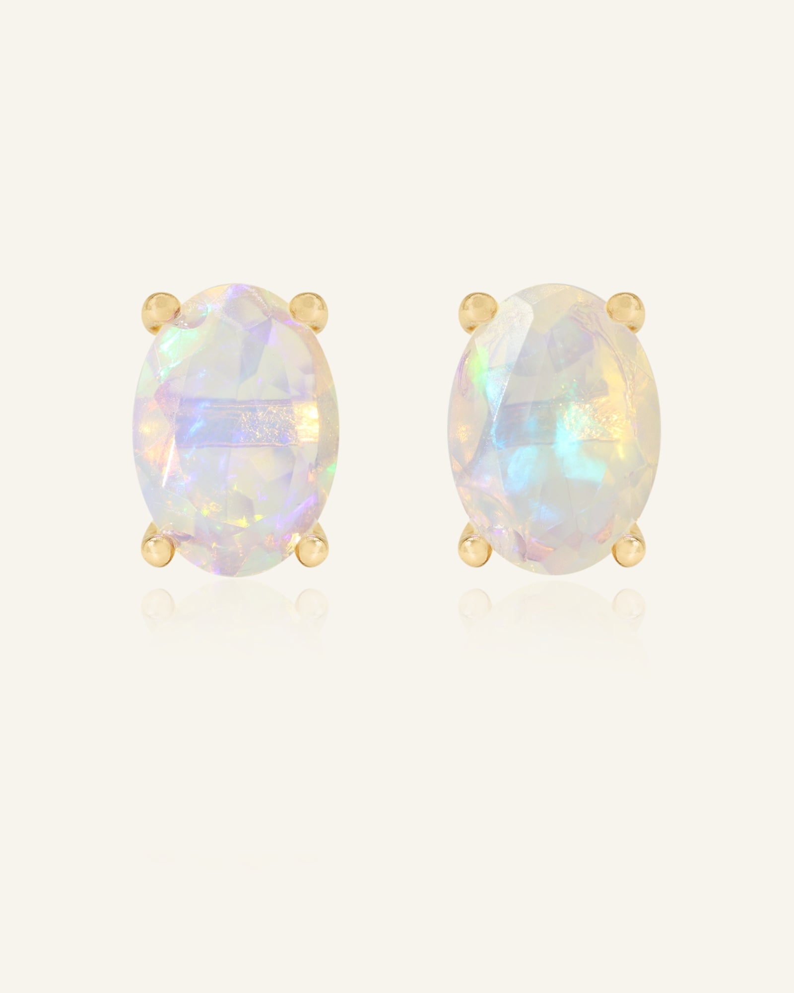 Prism Opal Studs in yellow gold, resting on a warm linen background