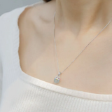 A model wearing the Fortune cat necklace featuring a silver pendant with a cheerful hand-painted cat perched atop a smooth blue chalcedony gemstone, symbolizing serenity and good fortune.