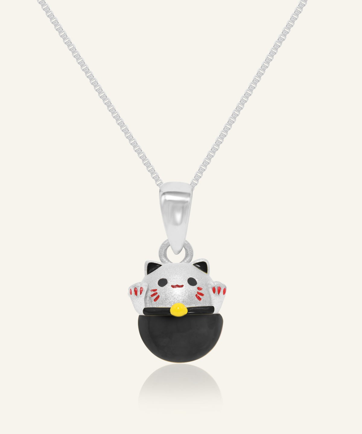 Fortune Cat Necklace (Obsidian) in silver, resting on a warm linen background