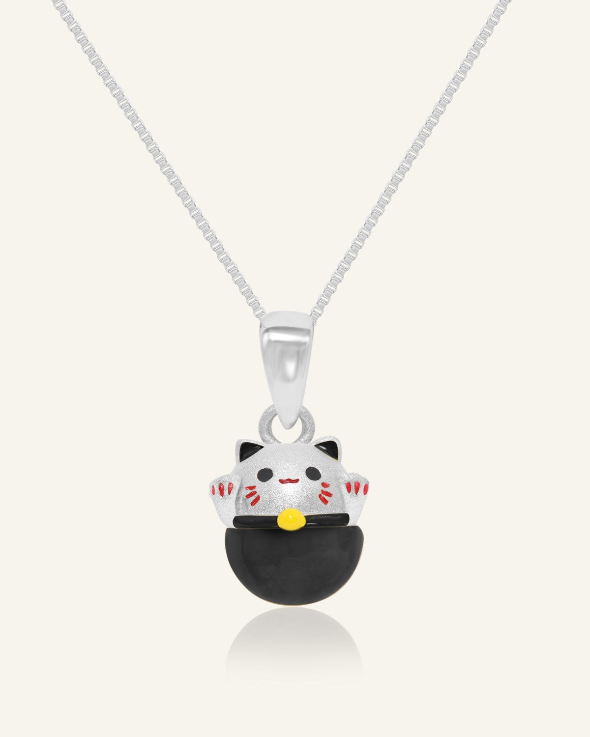 Fortune Cat Necklace (Obsidian) in silver, resting on a warm linen background