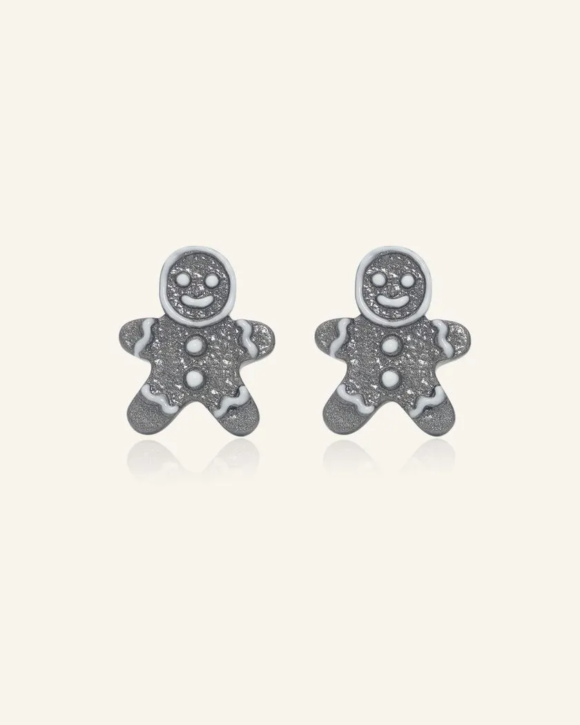 A pair of black gold earrings shaped like gingerbread men, adorned with sparkling details and white enamel accents.	