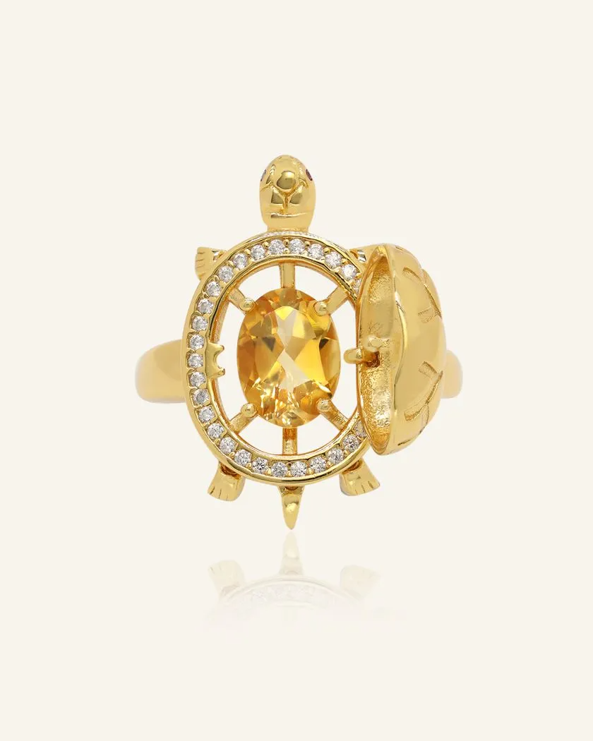 Close up of the Golden turtle ring with a hinged shell that opens to reveal a vibrant oval citrine gemstone at its center, surrounded by a sparkling halo of white stones, set in a polished gold band.