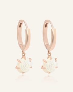 Close-up of the Handcarved White Shell Rose Huggies in rose gold, resting on a warm linen background