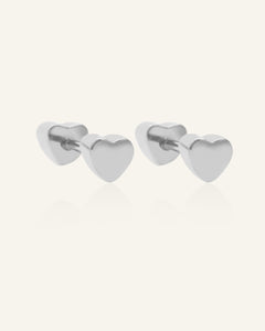 Close-up of the Heart Barbell Screwback Studs in silver, resting on a warm linen background
