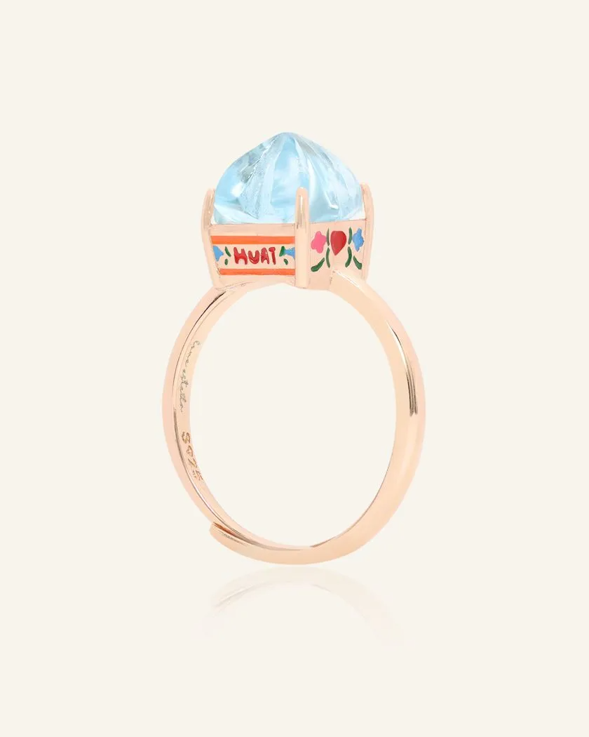 Rose Gold Huat Kueh-inspired ring featuring a vibrant sky blue topaz gemstone as the steamed cake centerpiece, adorned with intricate hand-painted enamel details, including 'Huat' and floral accents symbolizing prosperity and joy.