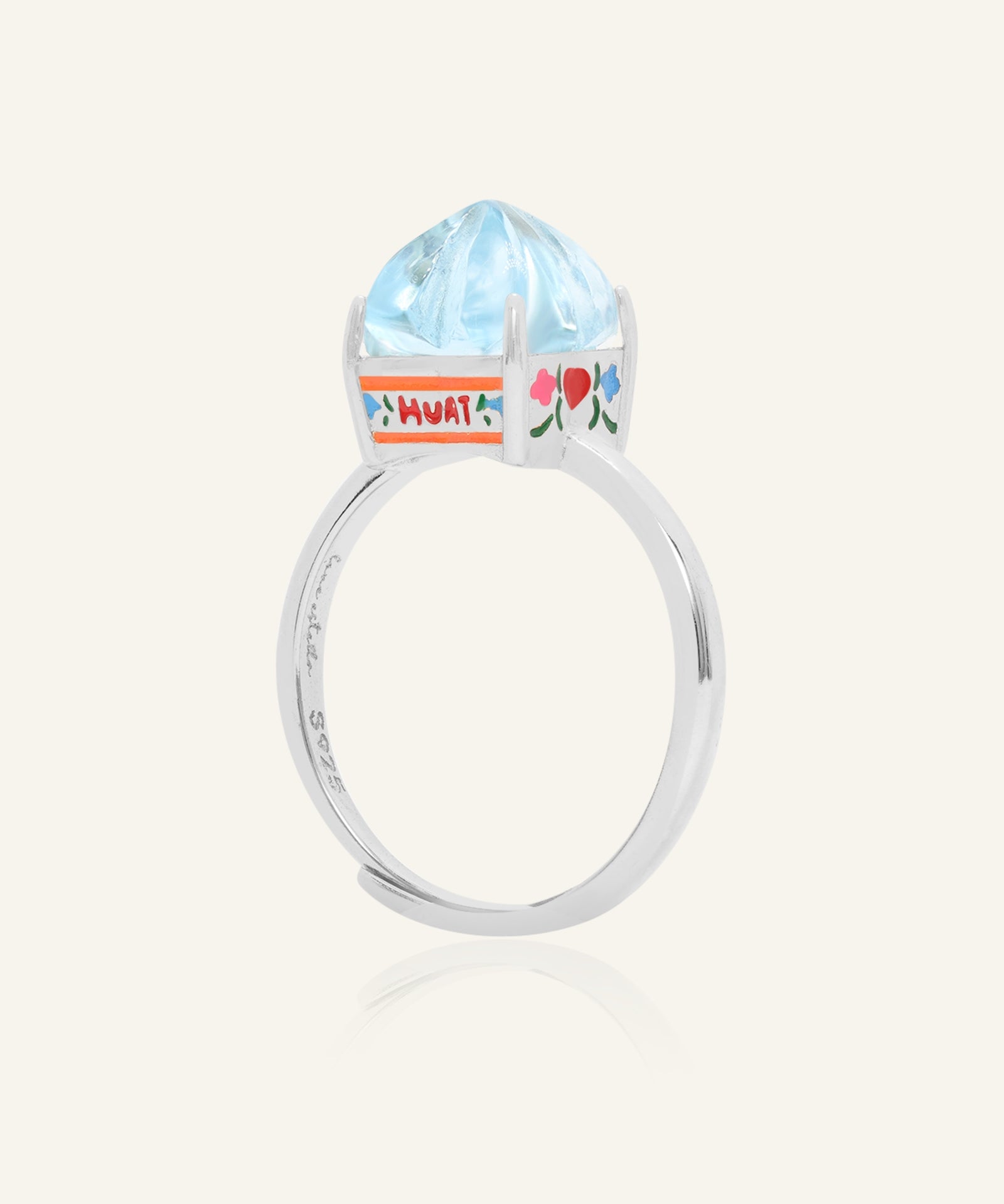 Close-up of the Huat Kueh Ring (Sky Blue Topaz) in silver, resting on a warm linen background