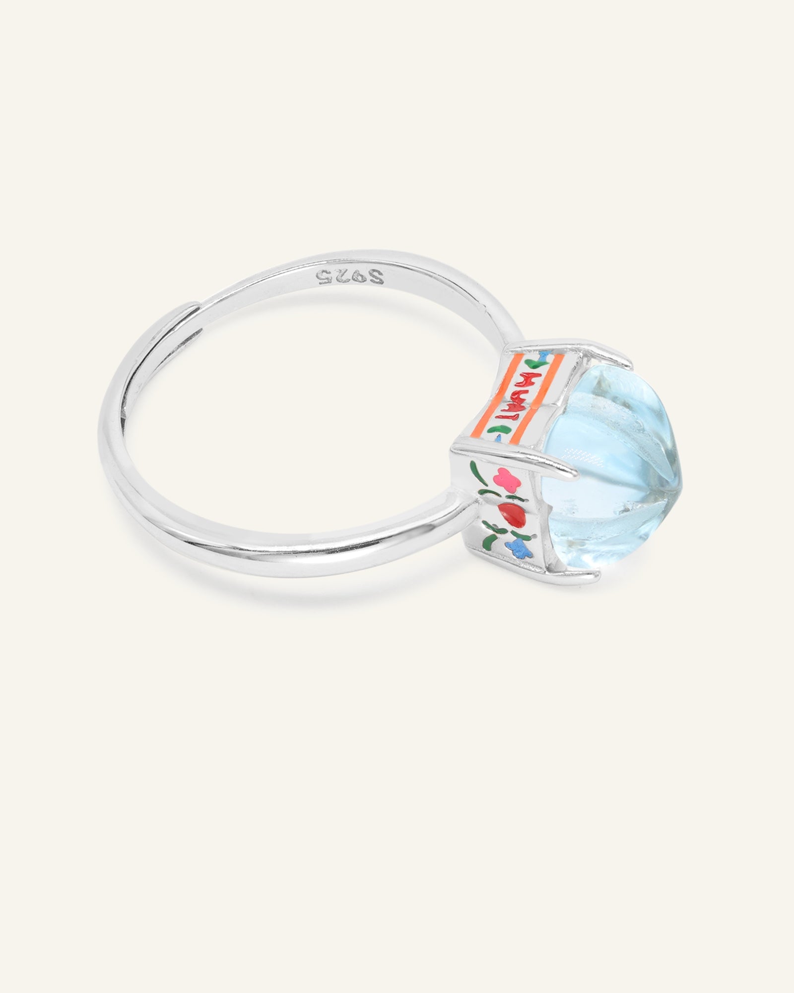 Huat Kueh Ring (Sky Blue Topaz) in silver, resting on a warm linen background, alternate angle