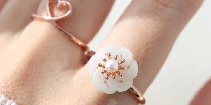 Rose gold jadeite knot ring worn on the finger, highlighting its subtle green hue and intricate knot design.		