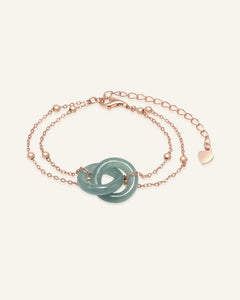 Jadeite Infinity Lock Bracelet in rose gold, resting on a warm linen background