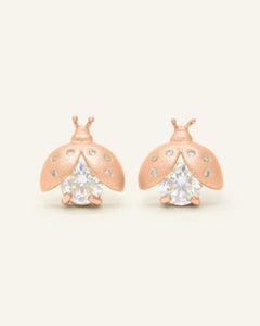Close-up of the Ladybug Studs | Moissanite in rose gold, resting on a warm linen background