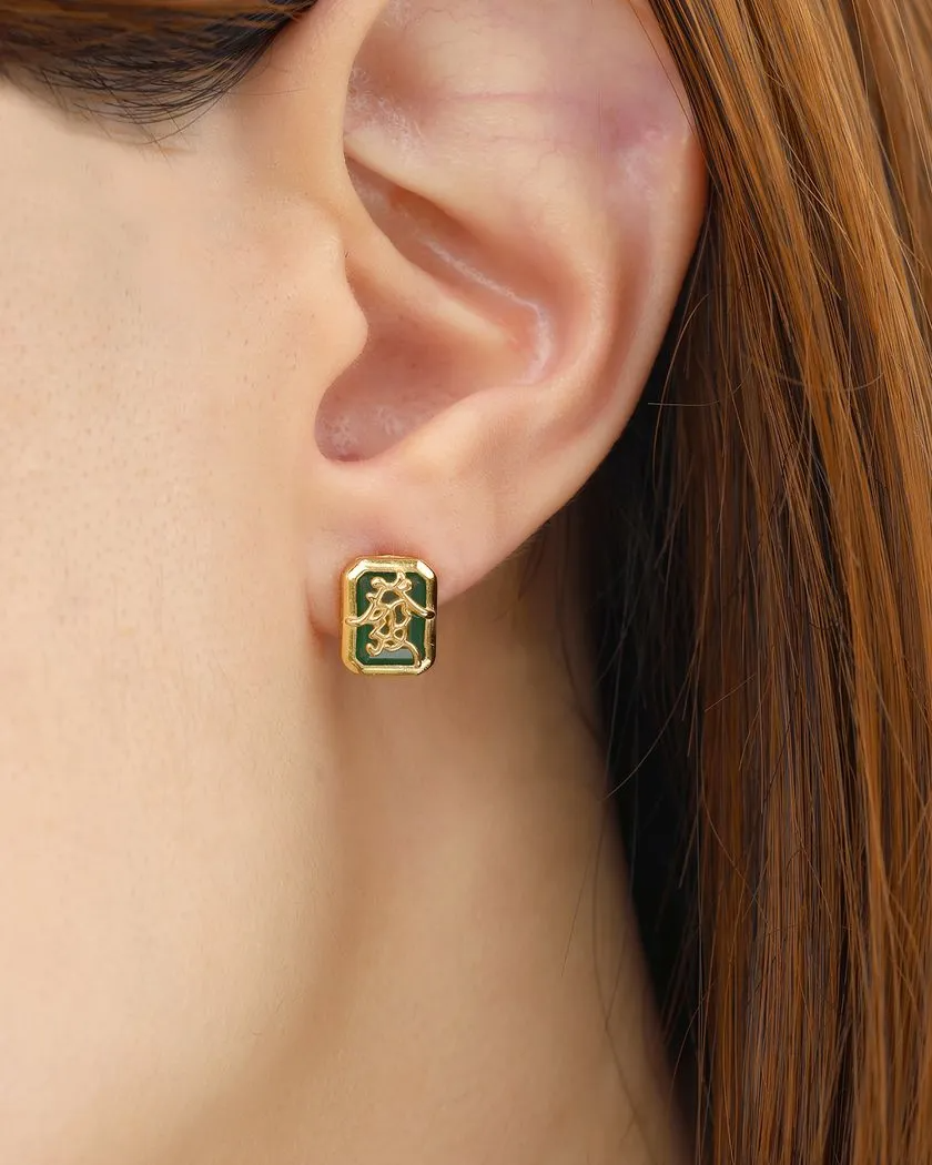 A model wearing a pair of mahjong-themed stud earrings set in yellow gold, featuring one stud with a red agate stone displaying the Hong Zhong (Red Dragon) tile, and the other with a green agate stone adorned with the Qing Fa (Green Dragon) symbol.