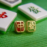 A pair of mahjong-themed stud earrings set in yellow gold, featuring one stud with a red agate stone displaying the Hong Zhong (Red Dragon) tile, and the other with a green agate stone adorned with the Qing Fa (Green Dragon) symbol.