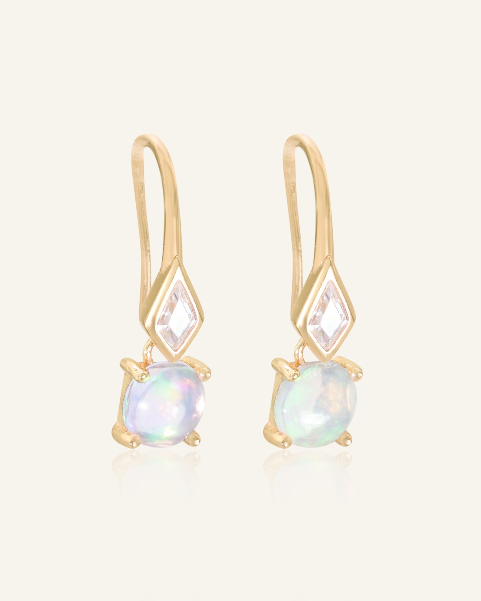 Atlas Opal Ear Drops in yellow gold, resting on a warm linen background