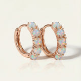 Close-up of the Lumi Opal Hoops in rose gold, resting on a warm linen background