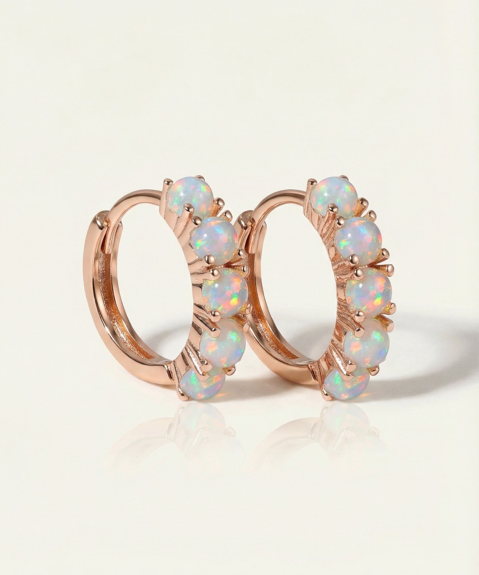 Close-up of the Lumi Opal Hoops in rose gold, resting on a warm linen background