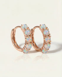Close-up of the Lumi Opal Hoops in rose gold, resting on a warm linen background