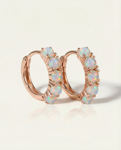 Close-up of the Lumi Opal Hoops in rose gold, resting on a warm linen background