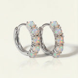 Lumi Opal Hoops in silver, resting on a warm linen background