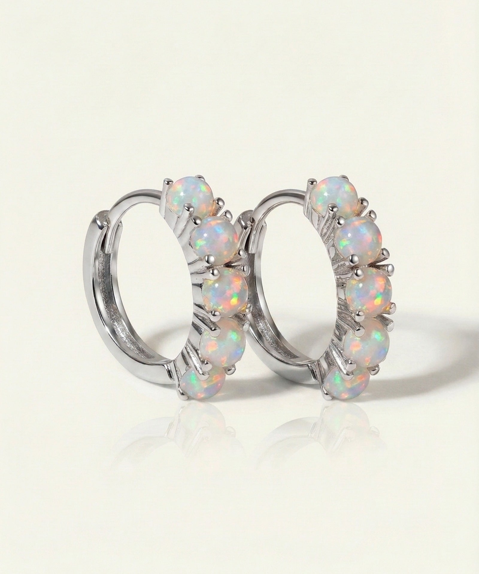 Lumi Opal Hoops in silver, resting on a warm linen background