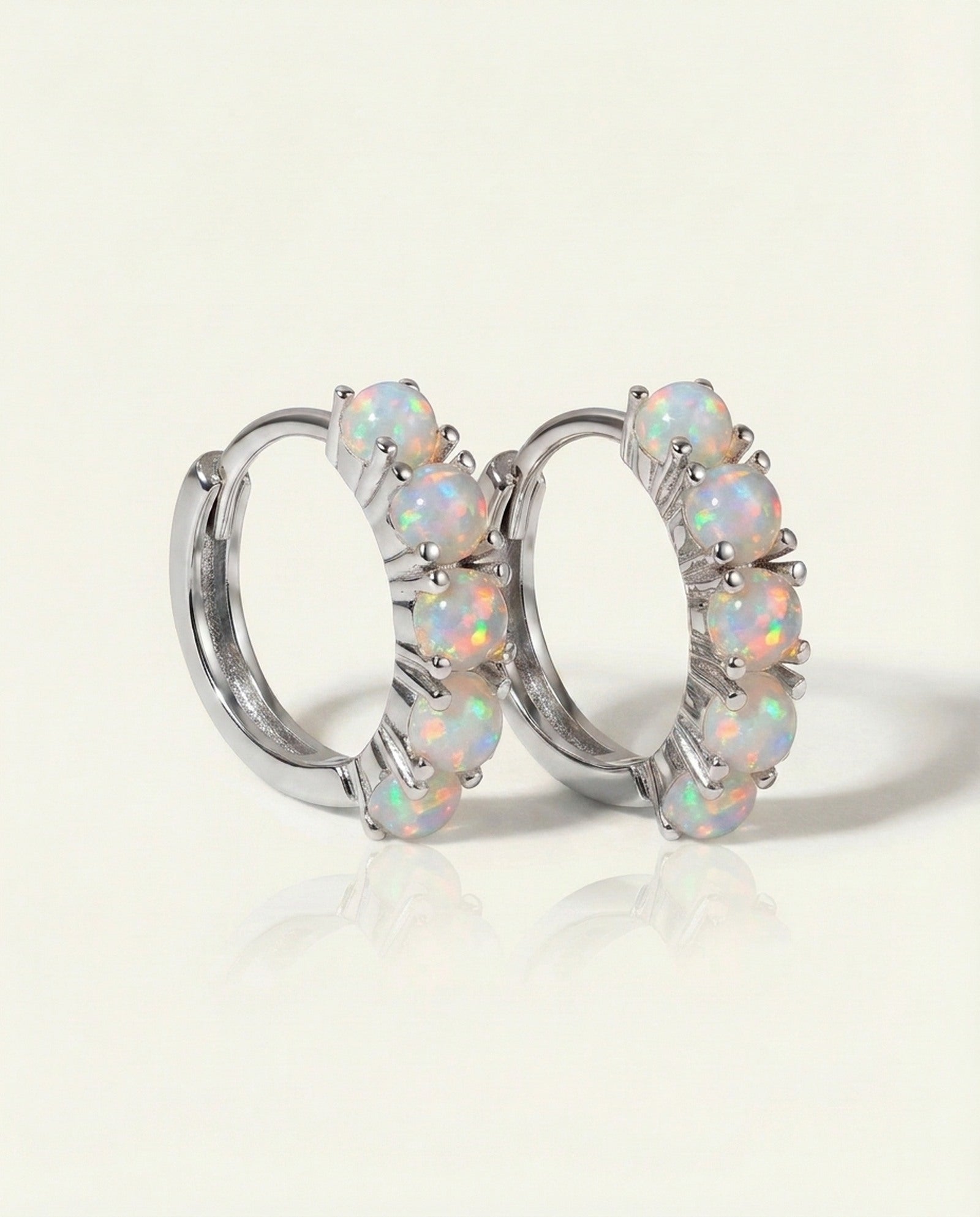 Lumi Opal Hoops in silver, resting on a warm linen background